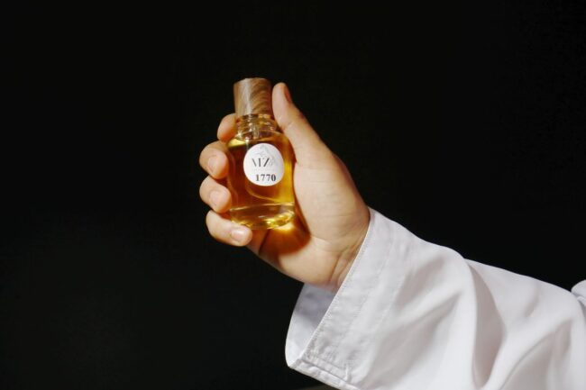 Mão segurando um frasco de perfume árabe dourado contra fundo escuro